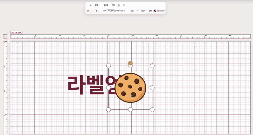 라벨 편집기 캔버스에 적용된 쿠키 클립아트를 드래그해 왼쪽으로 옮기고 크기를 키워 기존 텍스트 옆에 배치하는 화면.